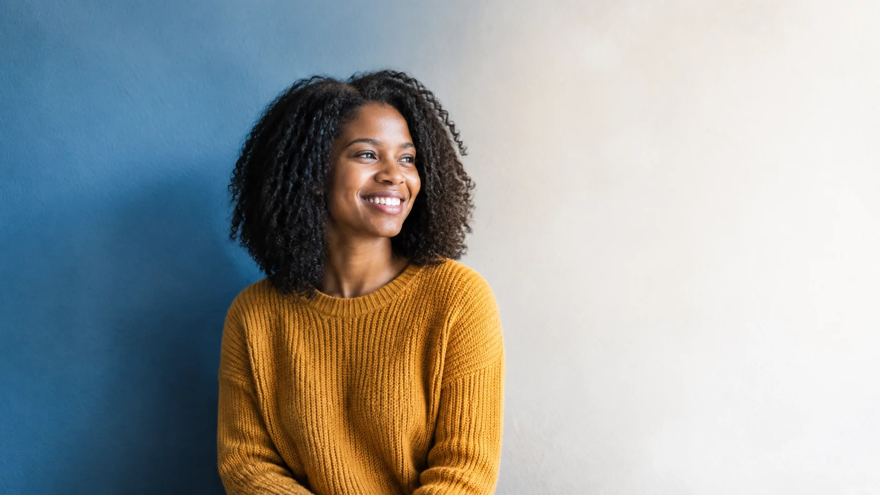 Smiling woman in a mustard sweater against a blue wall